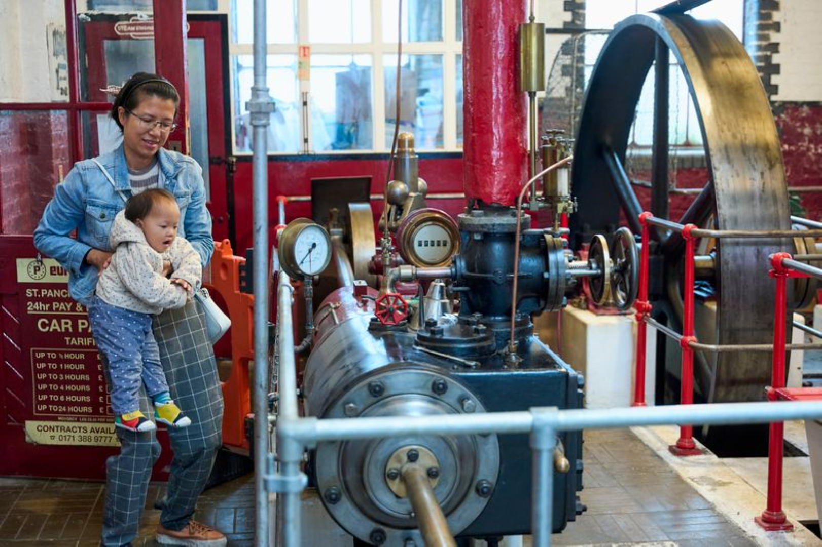 A mother and young child looking up at a vintage red and brass steam engine
